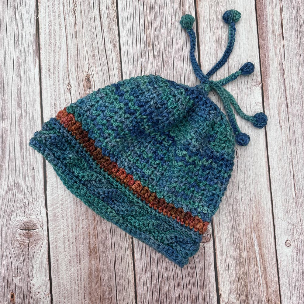 Cable brim hat with contrast band and crocheted pompom tassles.